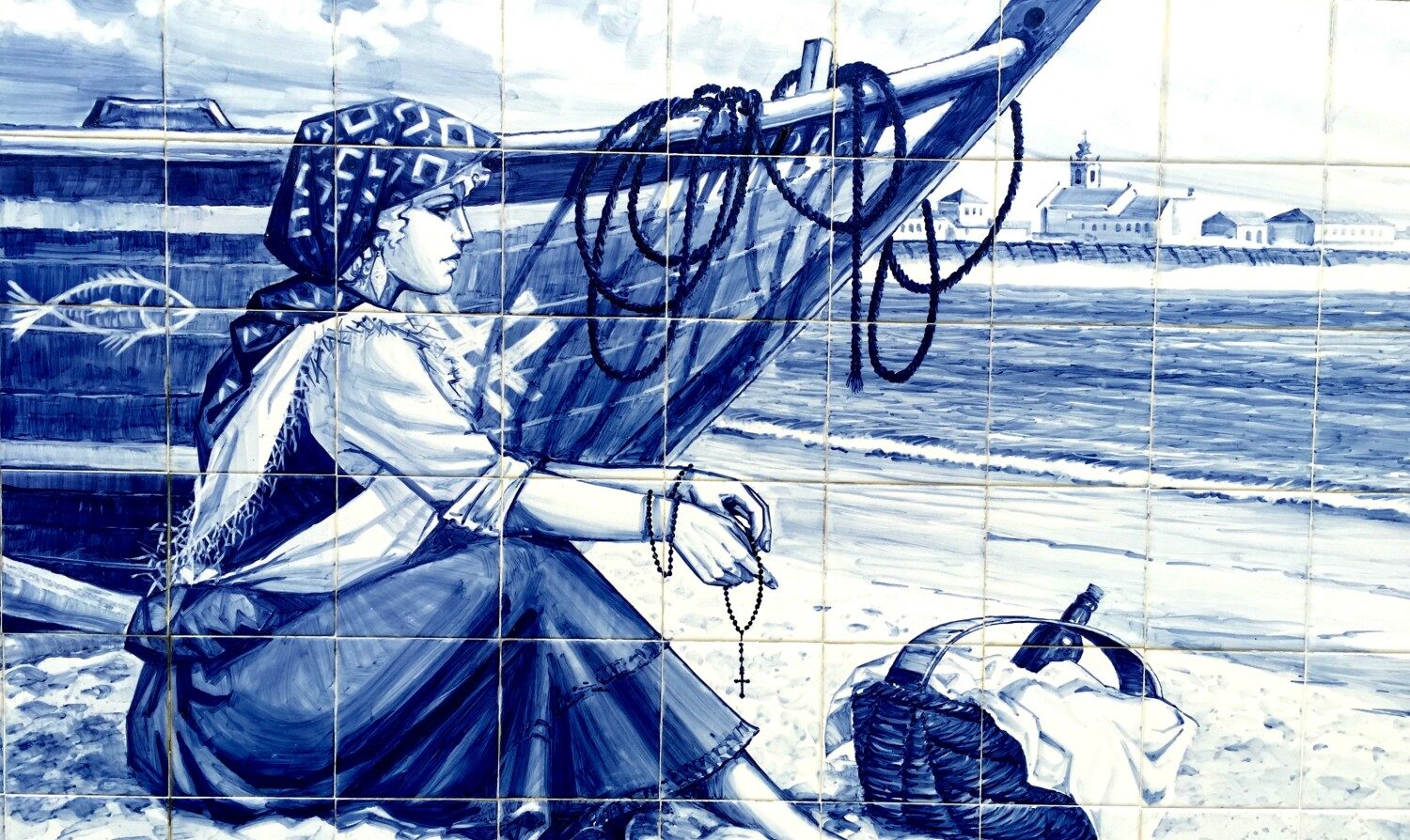 Azulejo tile mural of woman sitting in front of boat holding a rosary.