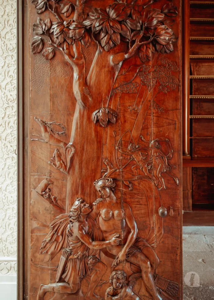 Wooden door with carvings of a large tree and people sitting beneath it.